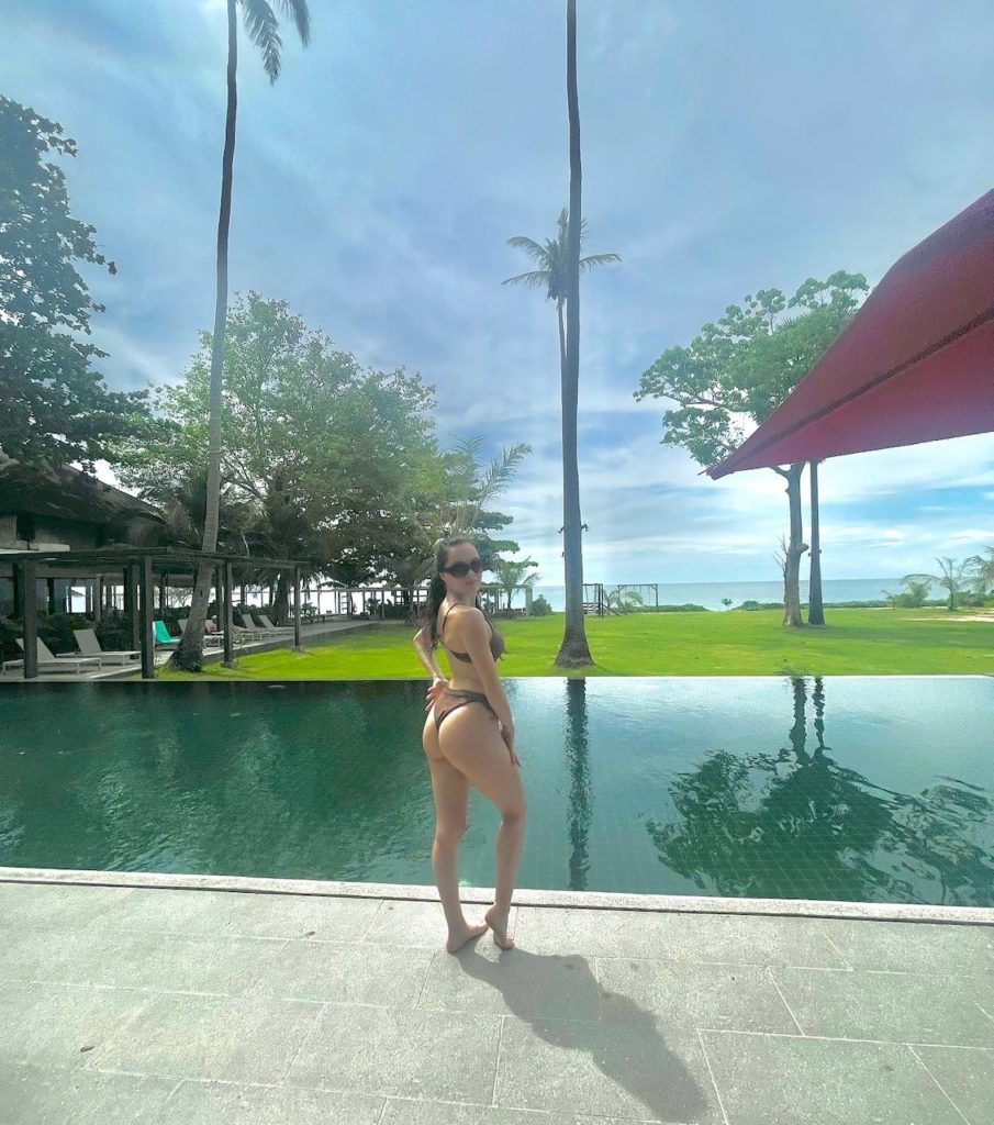 A woman in a bikini standing next to a pool, enjoying a sunny day by the water's edge.
