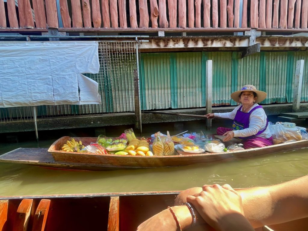 A Thai woman selling a range of fresh fruits on a wooden boat on a river.