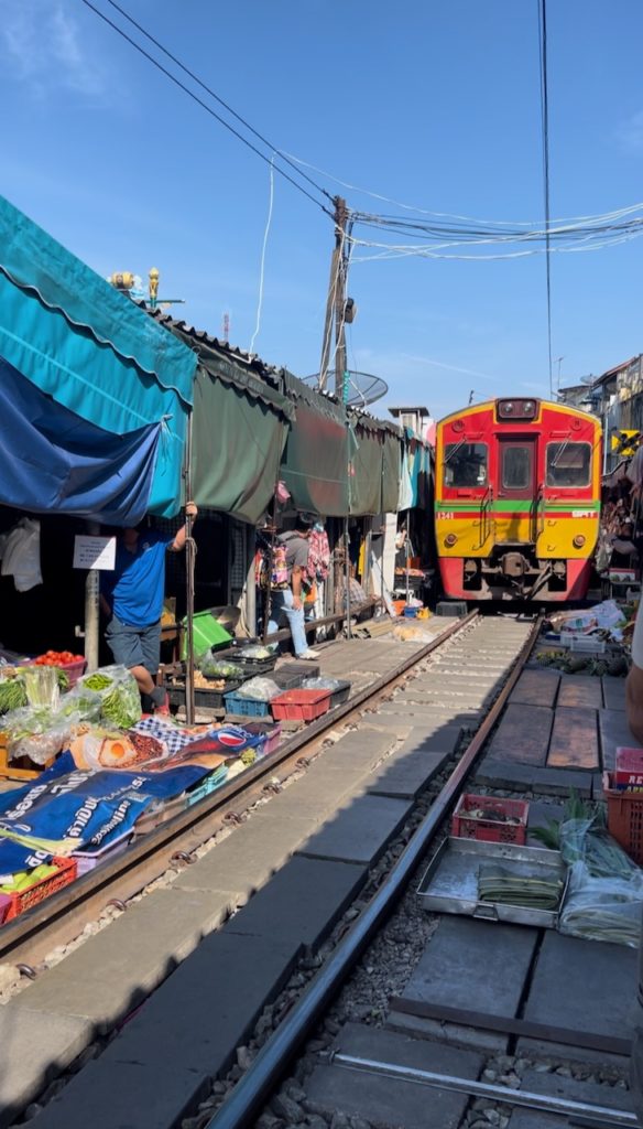 A red and yellow train travelling through a food market in Bangkok.