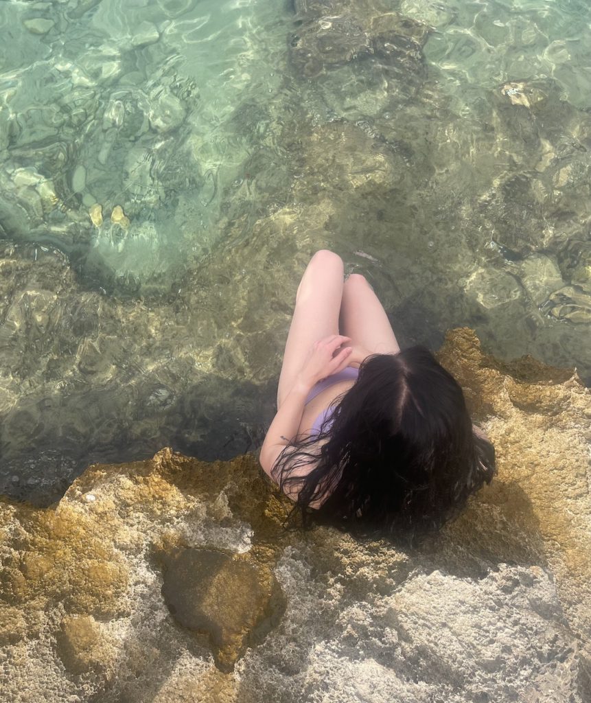 A woman sat in a natural rock seat in the clear blue sea of Spain.