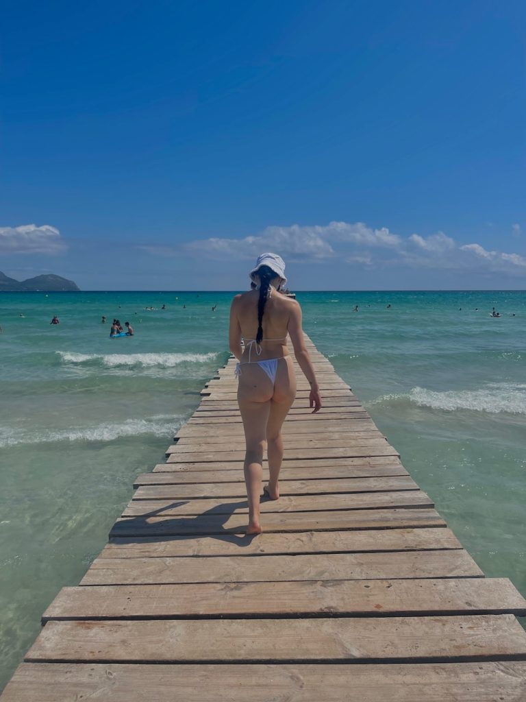 A woman strolling along a wooden pier on a bright sunny day over crystal blue ocean.