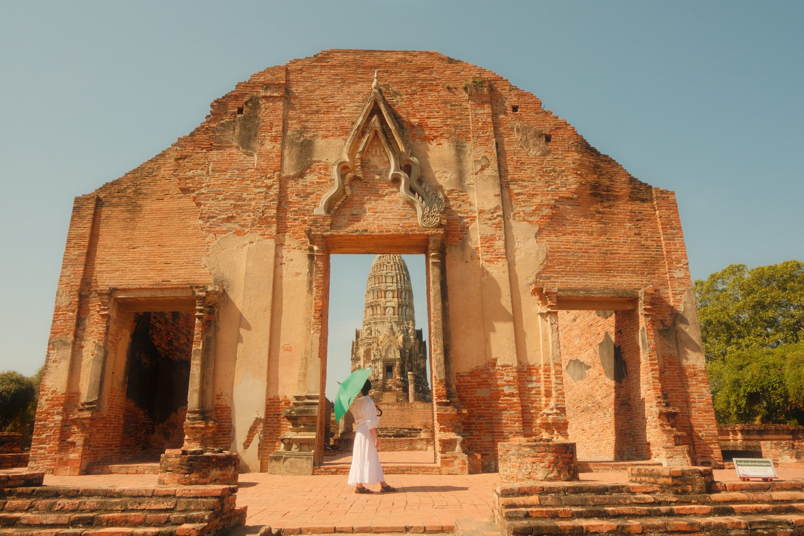 A woman posing with an umbrella to keep the intense sun off her at an ancient temple structure in Ayutthaya.