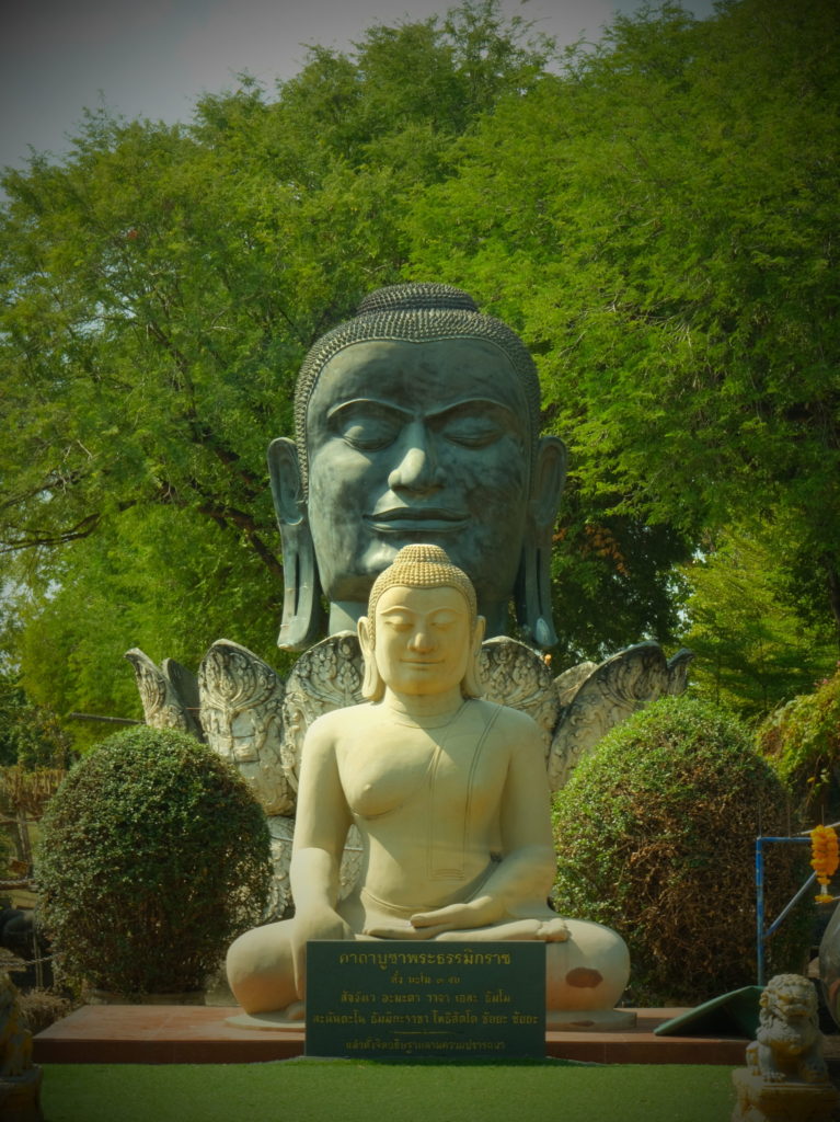 Two Buddha statues, one dark grey Buddha head emerging from a lotus flower and one cream coloured Buddha statue resting infront.