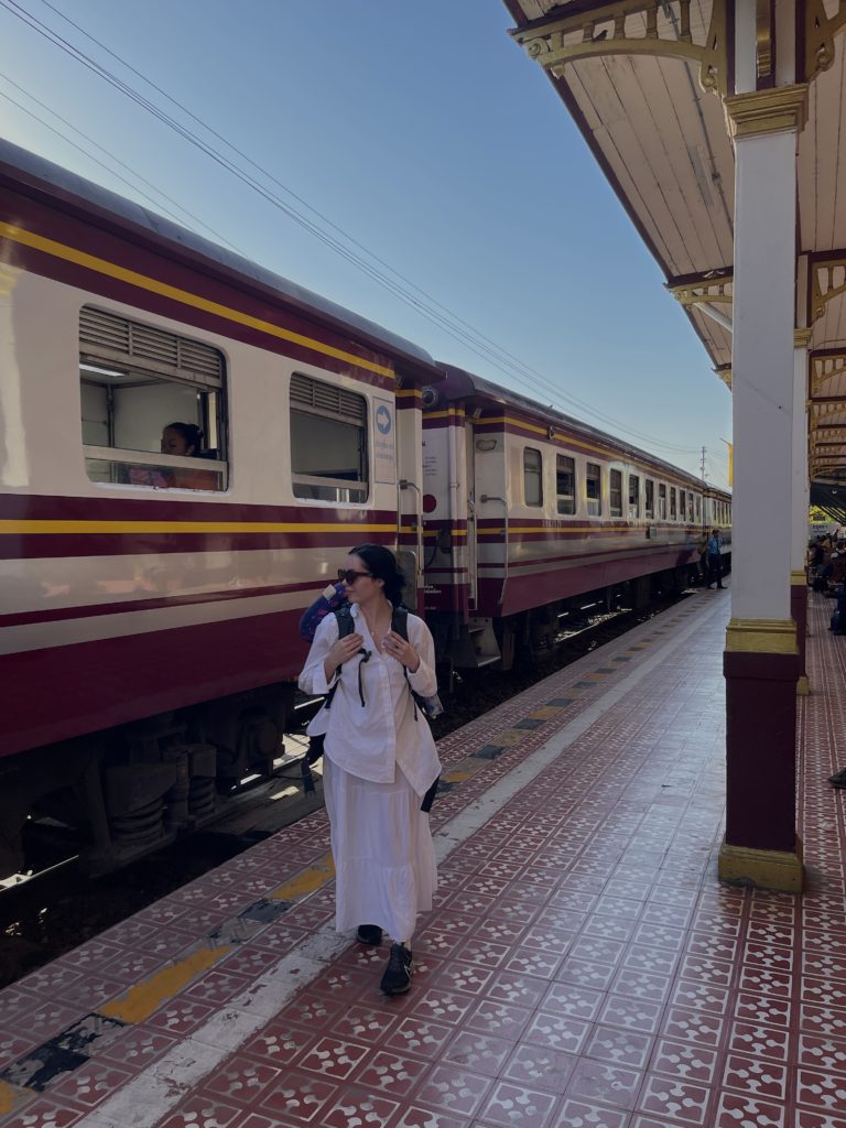 A backpacker stood on a platform next to an old school red, yellow and white striped train.