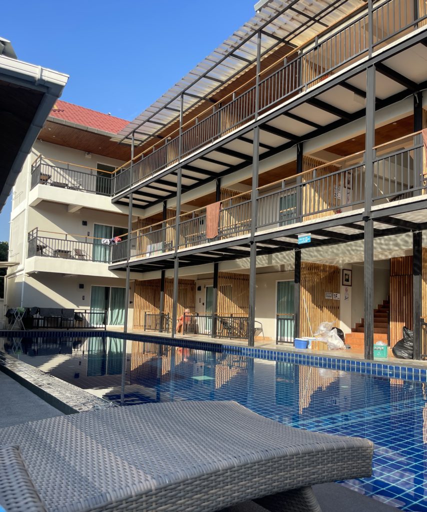 A hotel with a balcony, overlooking a pool with sunbeds.