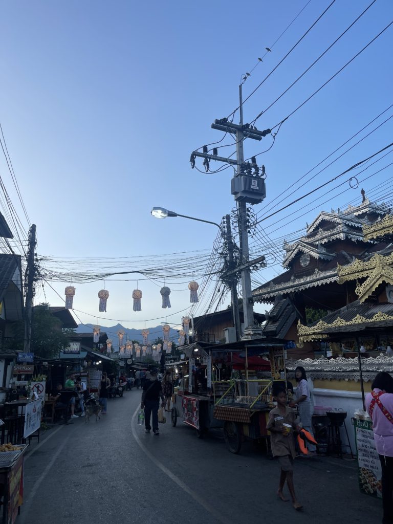A street full of street food vendors and a red and gold temple to the right.