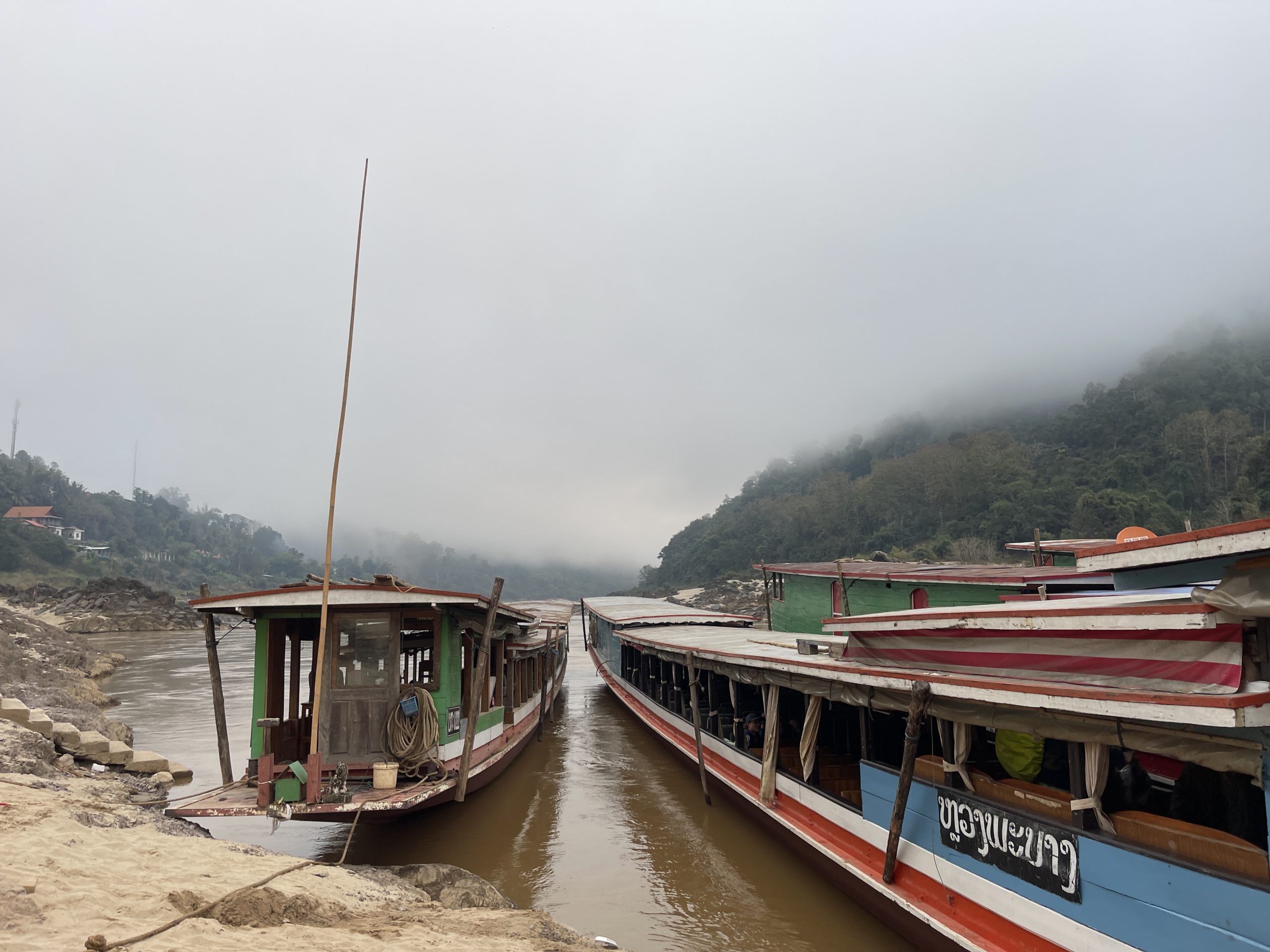Wooden slow boats surrounded by misty mountains on the Mekong River.