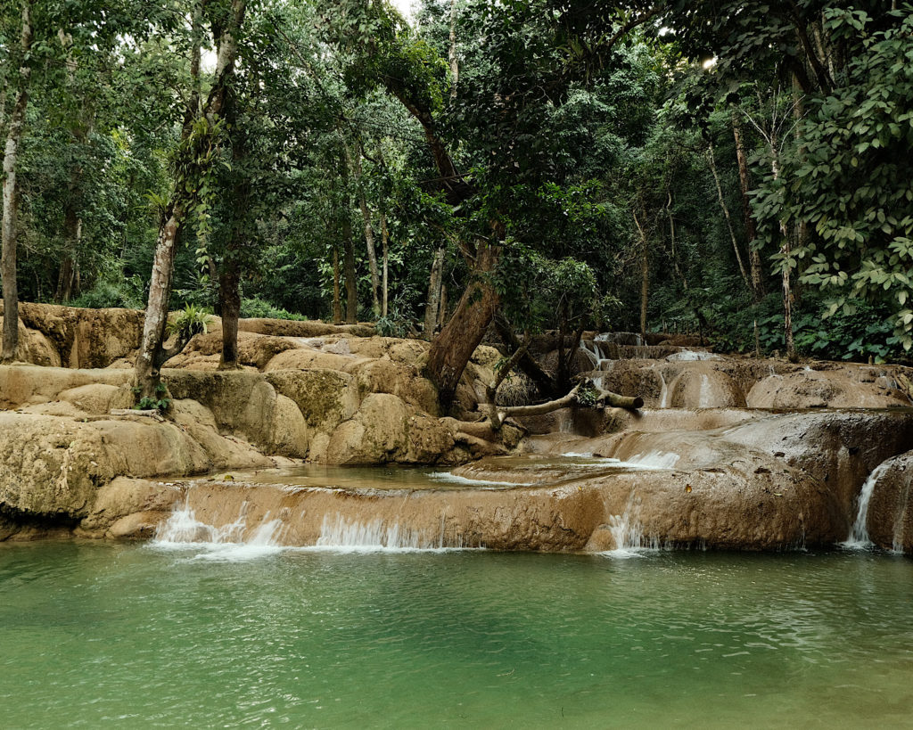 A cascading waterfall within a lush green jungle with an emerald pool.