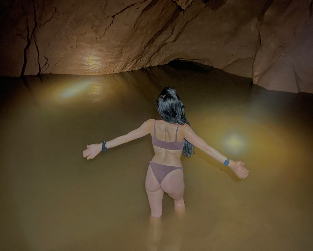 A woman standing in the water of a cave pool, illuminated by head torches.