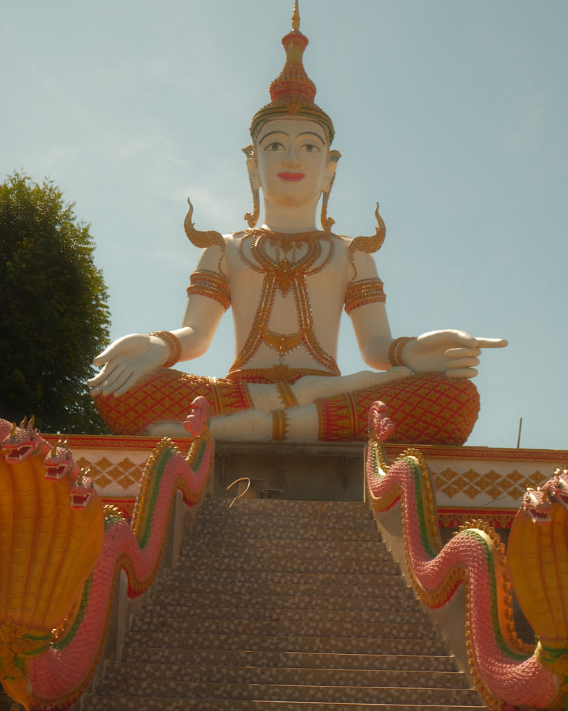 A large gold and red decorative Buddha statue seated above many steps.