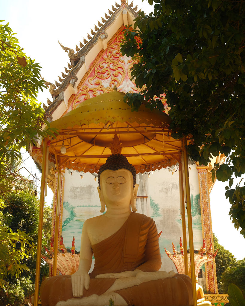 Buddha seated beneath a golden roof surrounded by trees.
