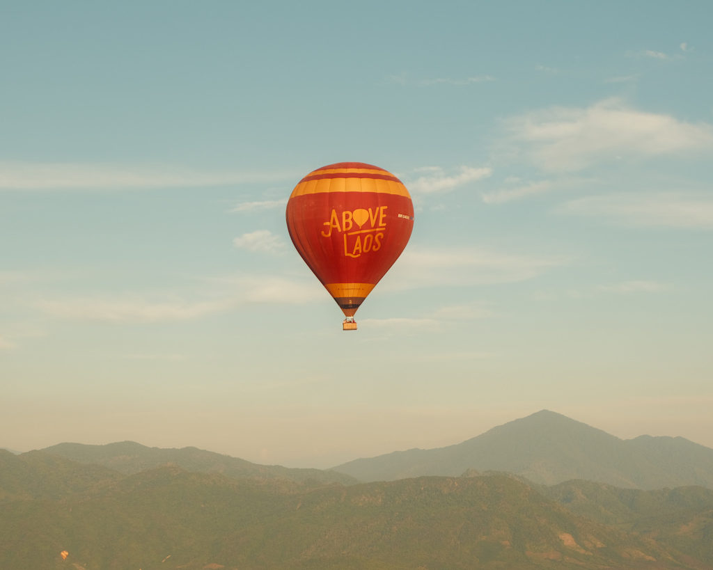 A red and yellow hot air balloon floating above the mountains.