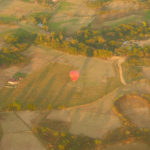 A red and yellow hot air balloon landing in countryside fields.