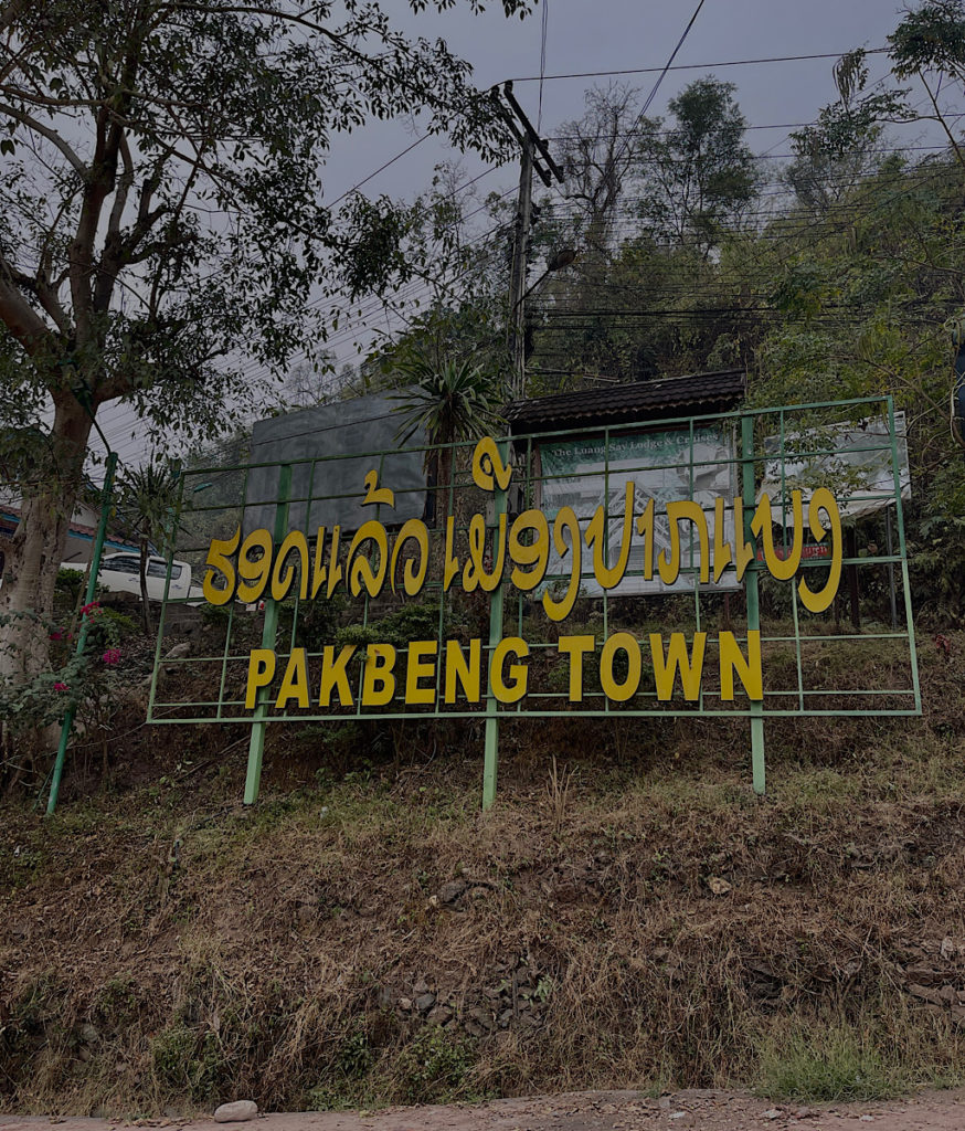 A yellow town sign surrounded by trees.