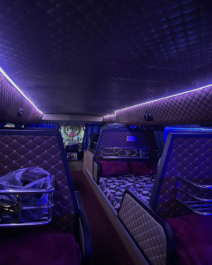 The inside of a sleeper bus with bright purple LED lighting and double beds to sleep on.