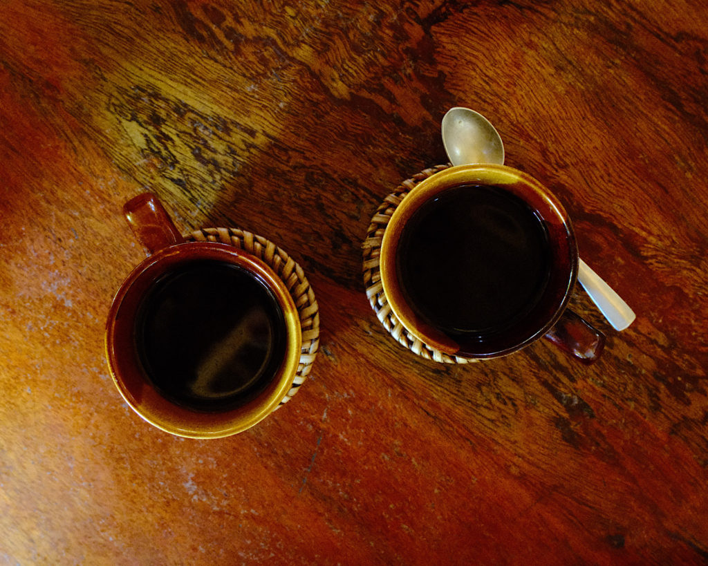 Two cups of black coffee on a wooden table with a teaspoon.