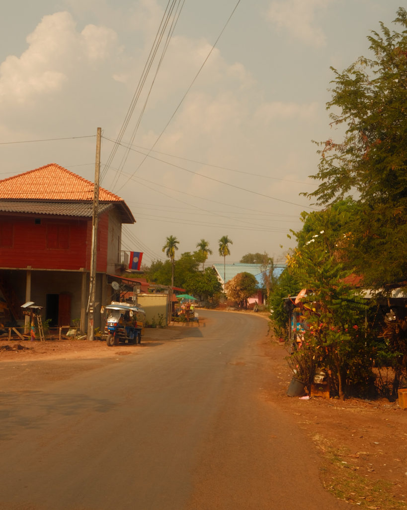 A scenic dirt road winding through a remote village on the Pakse loop, creating a rustic and remote atmosphere.