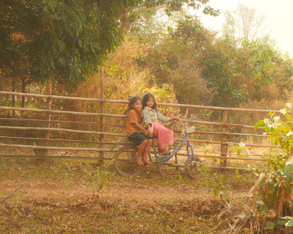 Two young girls happily riding a bike through a picturesque field.
