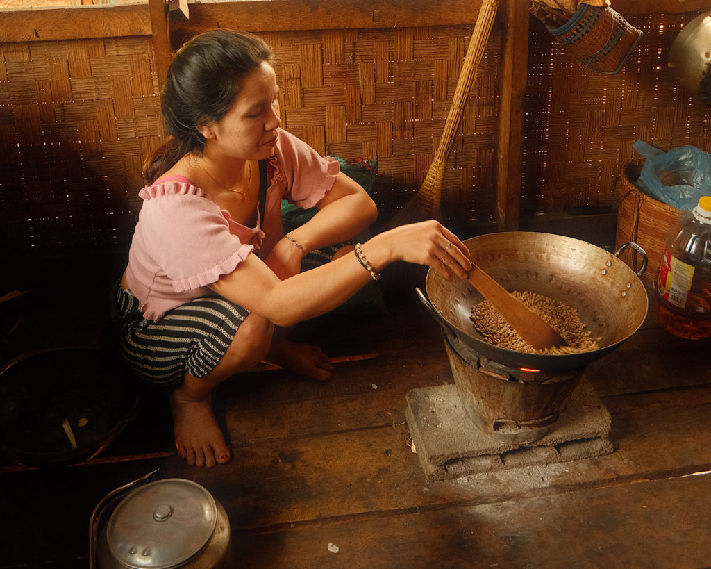 A woman perched on a wooden floor stirring coffee beans.