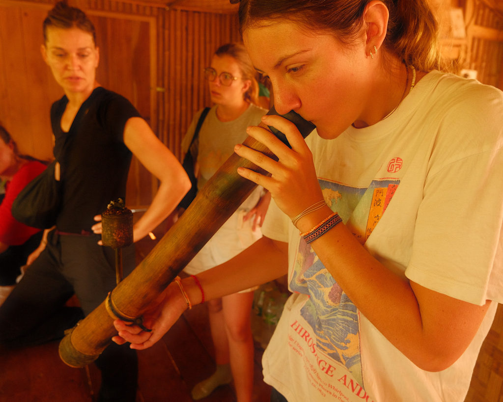 A tourist taking a pull from a bamboo bong filled with tobacco and sugar cane during an ethnic village tour.