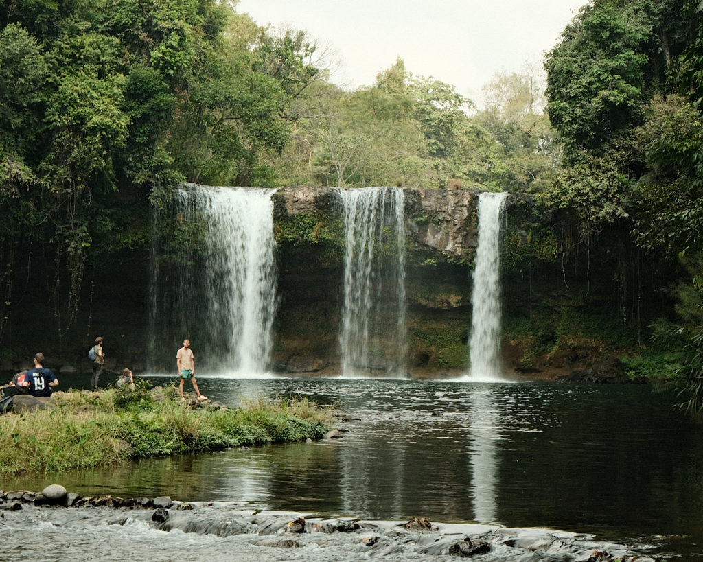 A pretty waterfall surrounded by fresh green vegetation with a large pool for swimming.