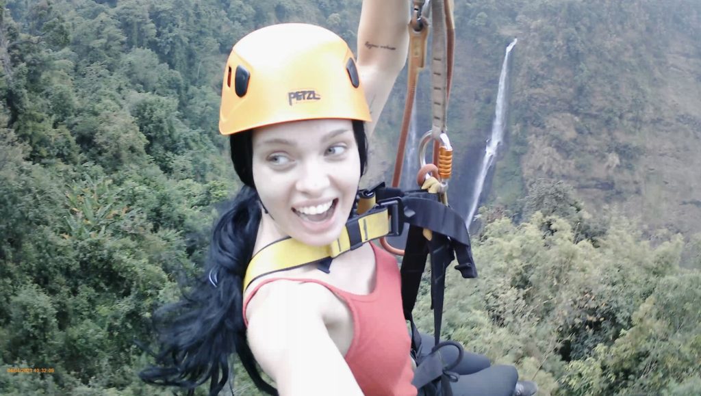 A woman ziplining over an incredible waterfall in the lush jungle.