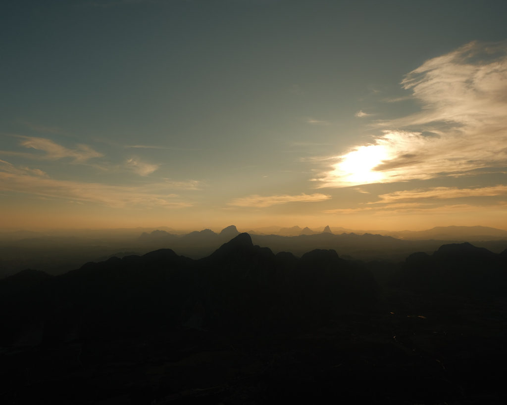 Sunset over majestic mountains, causing an orange glow on the peaks and creating a serene and breathtaking view from above.