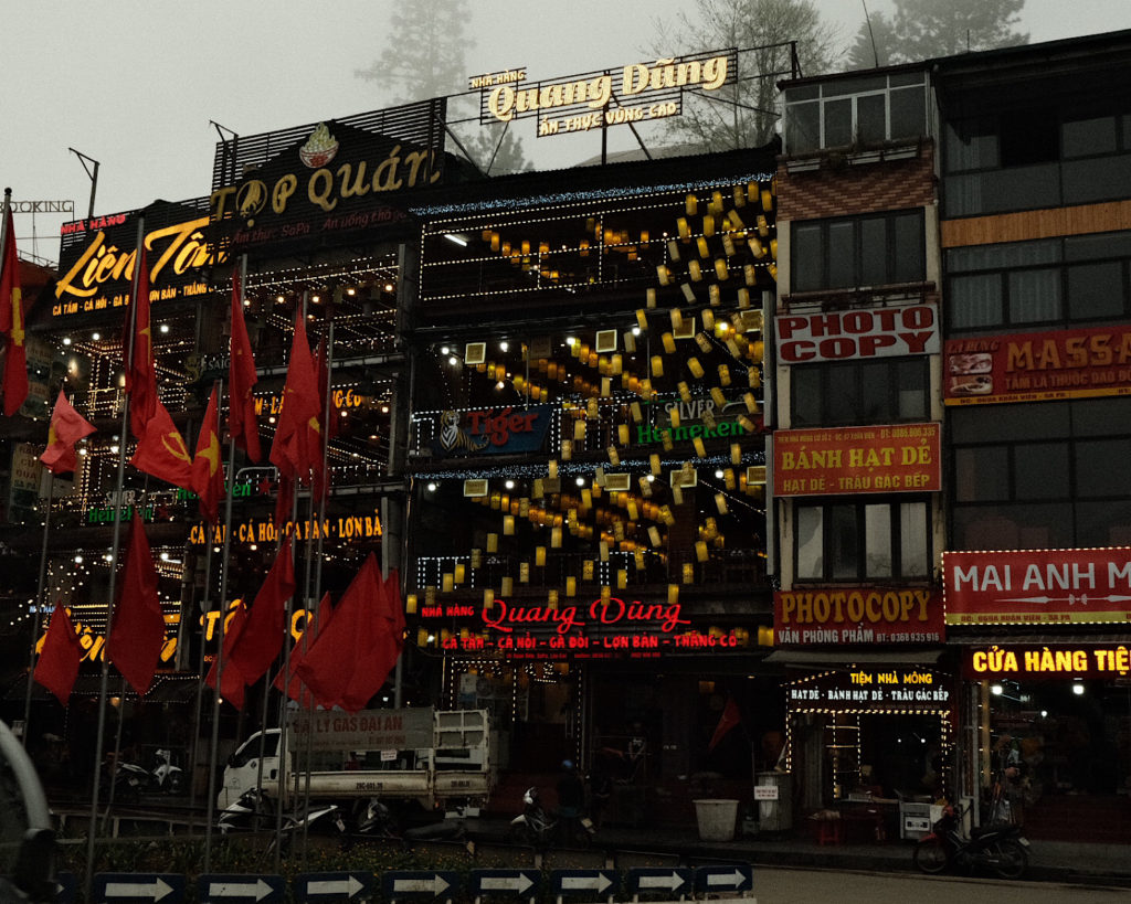 A bustling street lined with restaurants decorated with yellow lanterns.