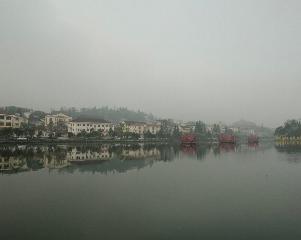 A foggy day with buildings in the distance, overlooking a serene lake.