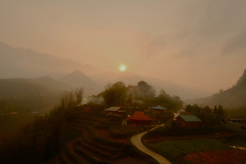A picturesque mountain village at sunset, with the sun casting a warm glow on the surrounding landscape.