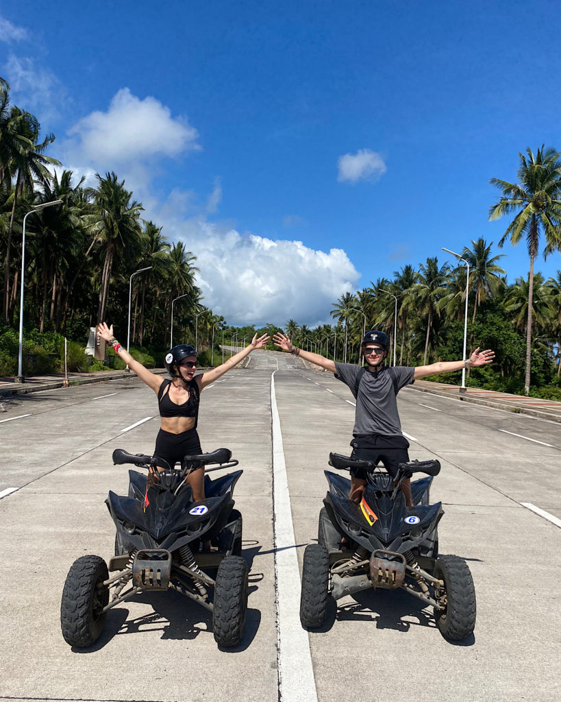 A couple riding ATVs on a huge road lined with palm trees.