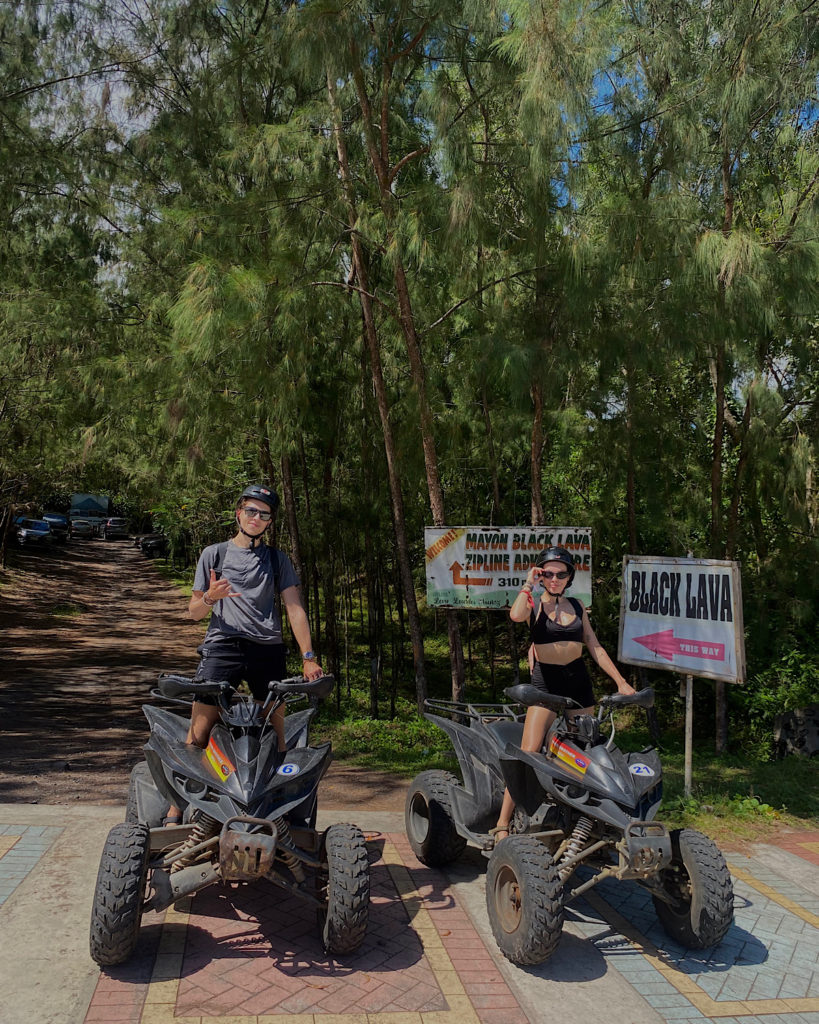 Two people riding ATVs surrounded by trees.