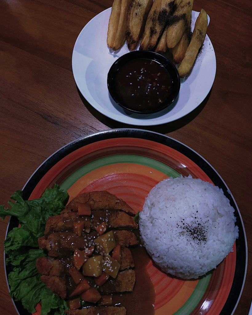 A plate of katsu chicken curry and a side plate of thick potato wedges with sauce.