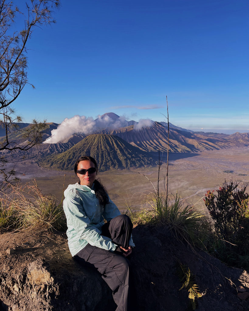 A woman sitting on a rock, gazing at Mount Bromo in the distance.