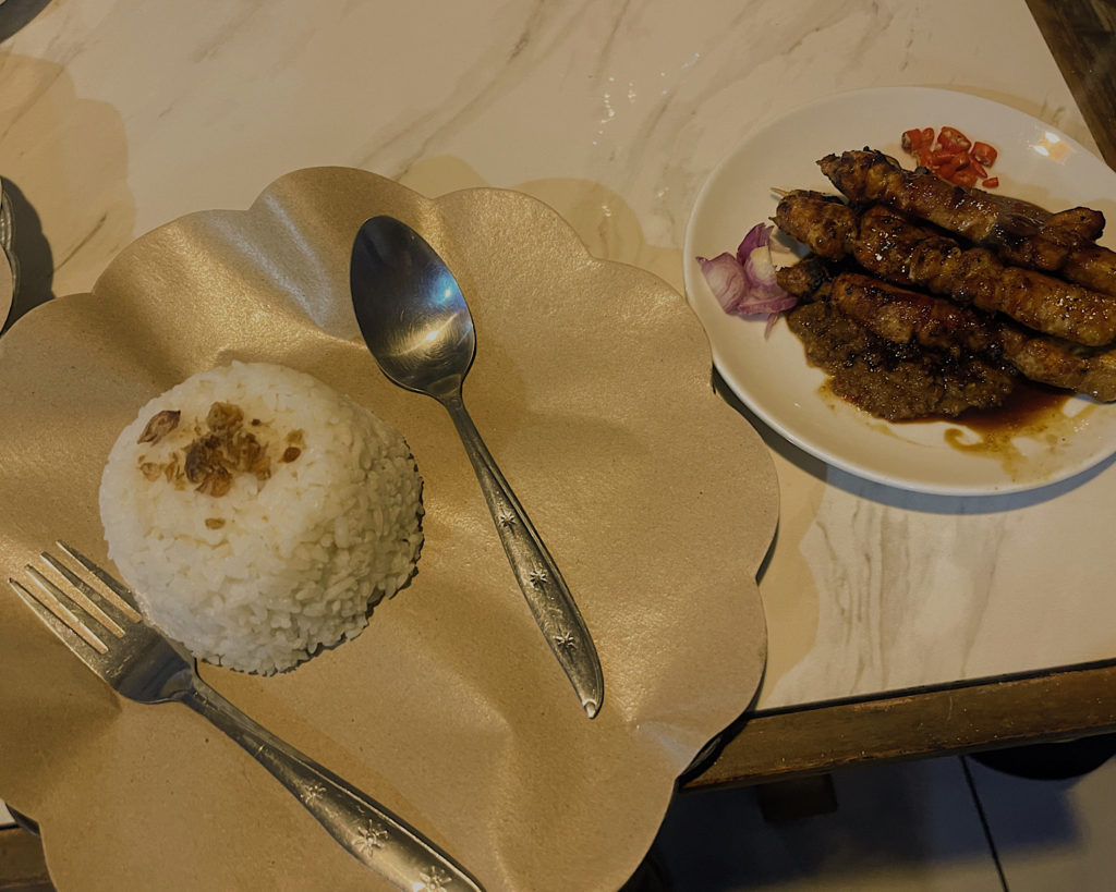 A dish of satay and rice on a table with silver cutlery.