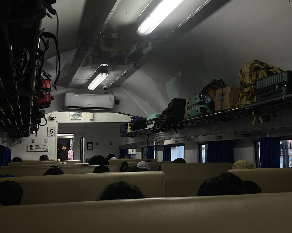 The inside of a local Indonesian train with lots of luggage stored above on the racks.