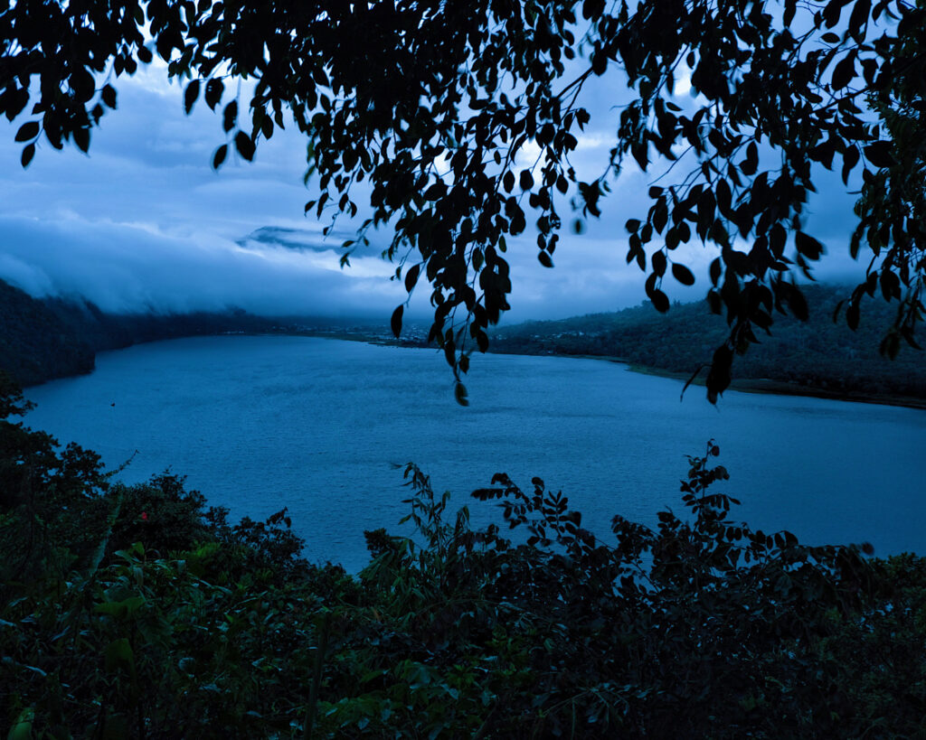 A serene lake nestled among lush trees with billowing clouds in the sky.