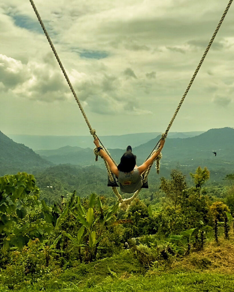 A woman swinging over the lush greenery of Munduk Bali's jungle.