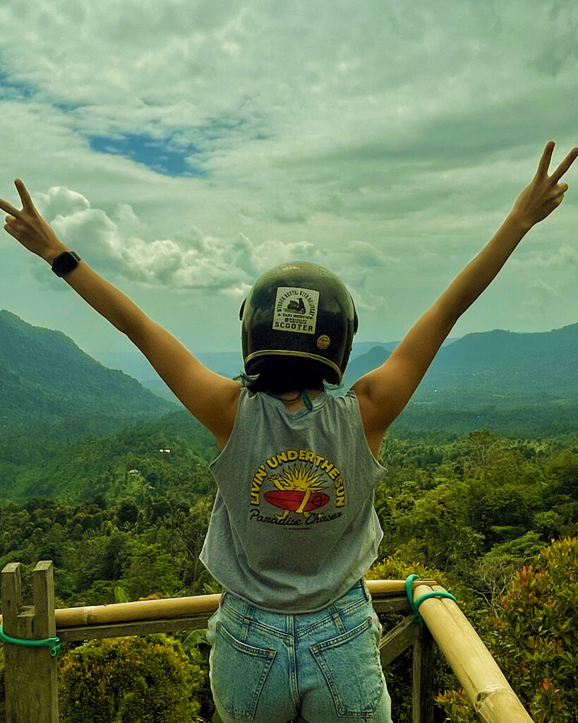 A woman wearing a motorbike helmet posing on a platform overlooking the jungle and mountains.