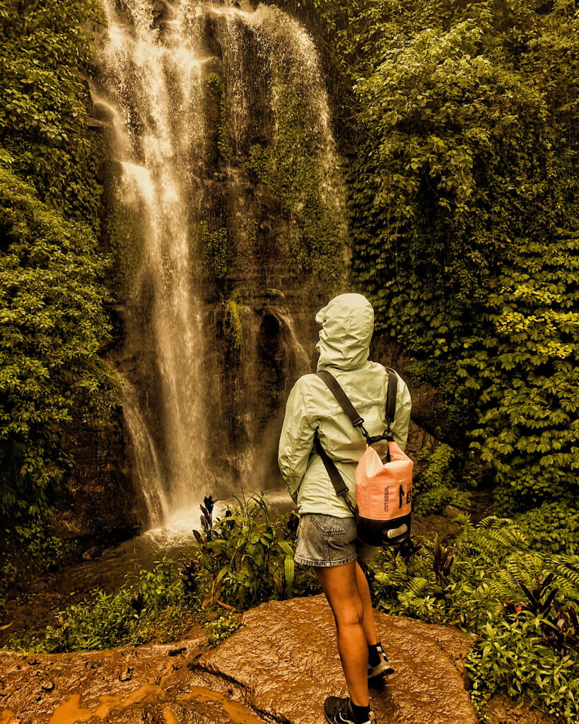 A woman in a raincoat standing in front of a gushing waterfall in the rain.