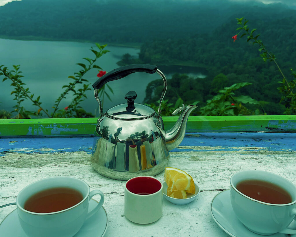 A teapot and tea cups on a rustic table overlooking a serene lake.