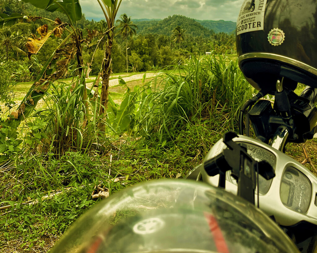 A motorbike with two helmets rested on the handles, parked in front of vibrant green rice paddies.