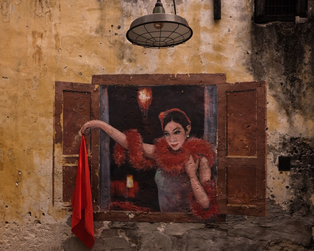 A street mural depicting a woman gracefully holding a vibrant red scarf.