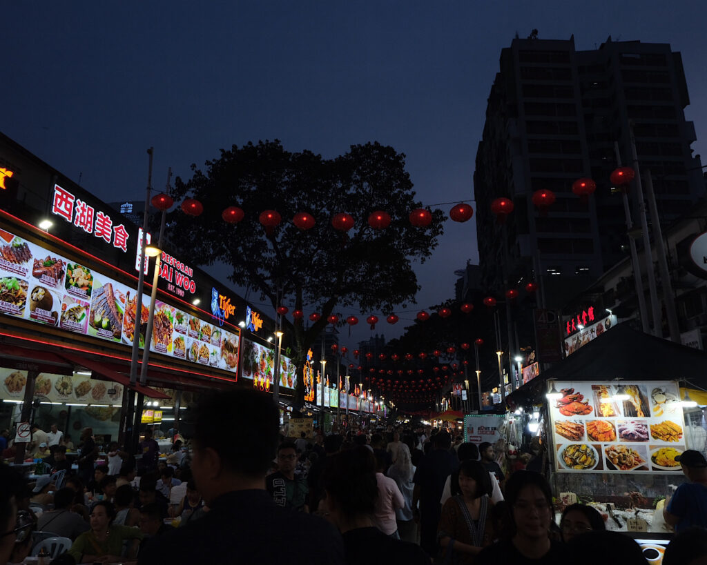 A bustling night market with large crowds amongst the vibrant lighting.