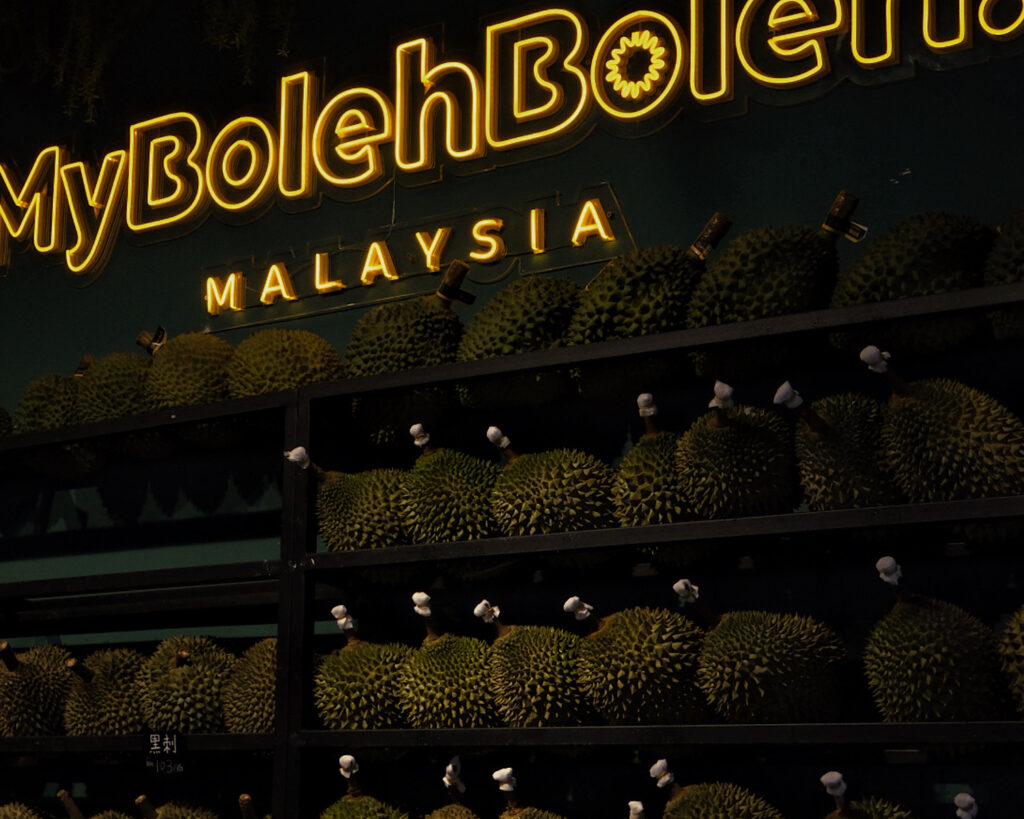 A bright neon yellow sign with dozens of durians lined on shelves below.